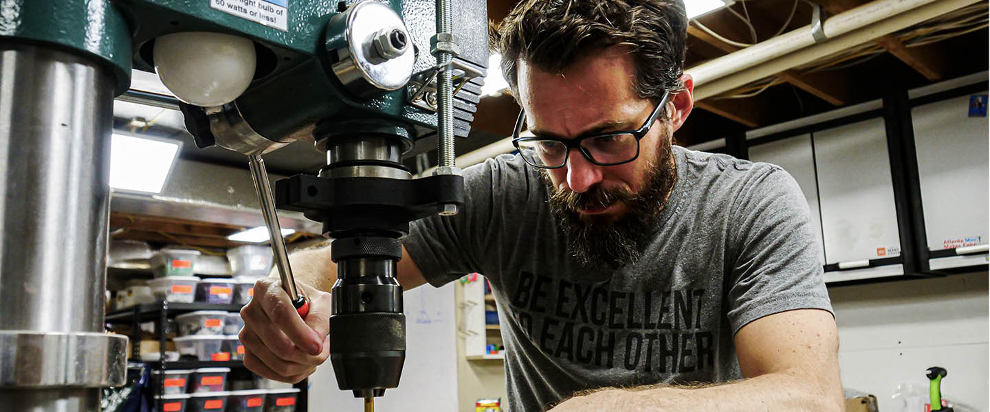 YouTube Creator Bob Clagett concentrates on using a drill press during a US Navy mystery shelter construction challenge