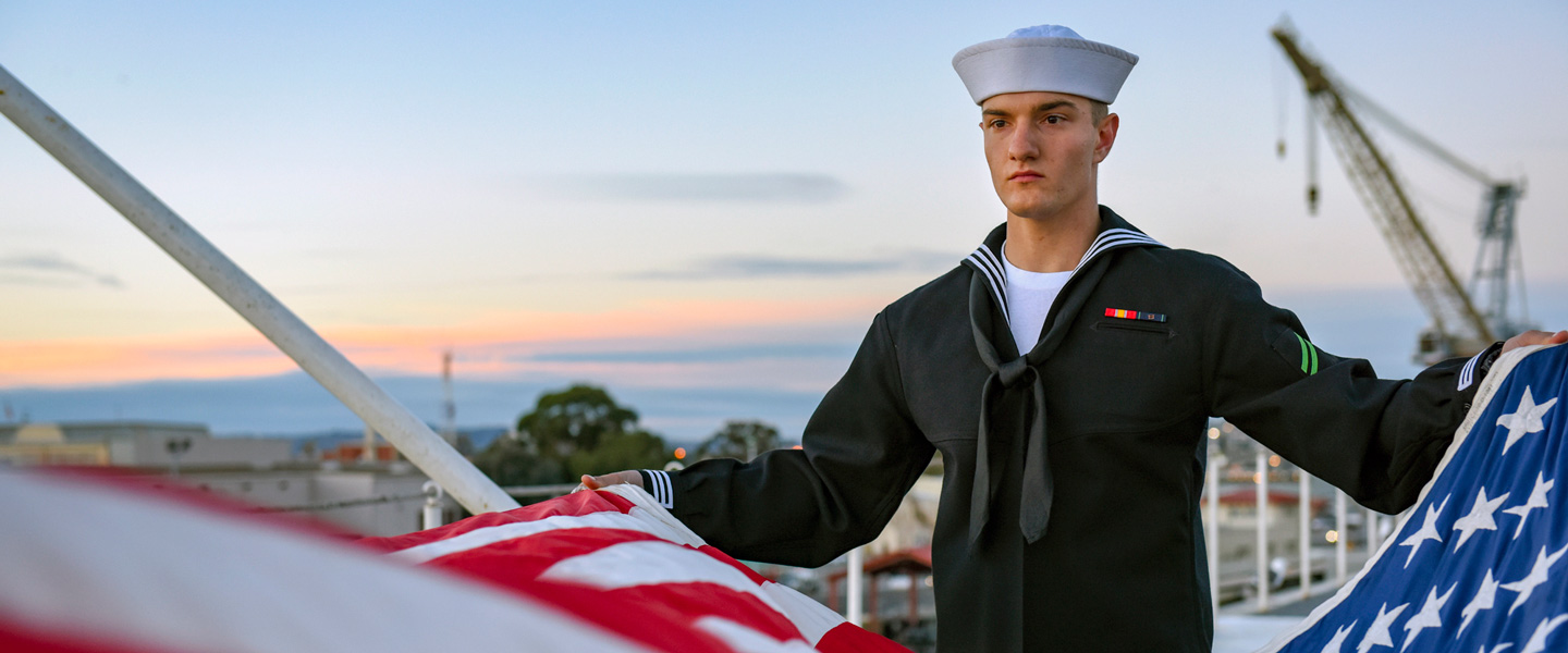 A Navy Sailor helps fold the United States flag during an evening colors ceremony aboard a Navy ship. 