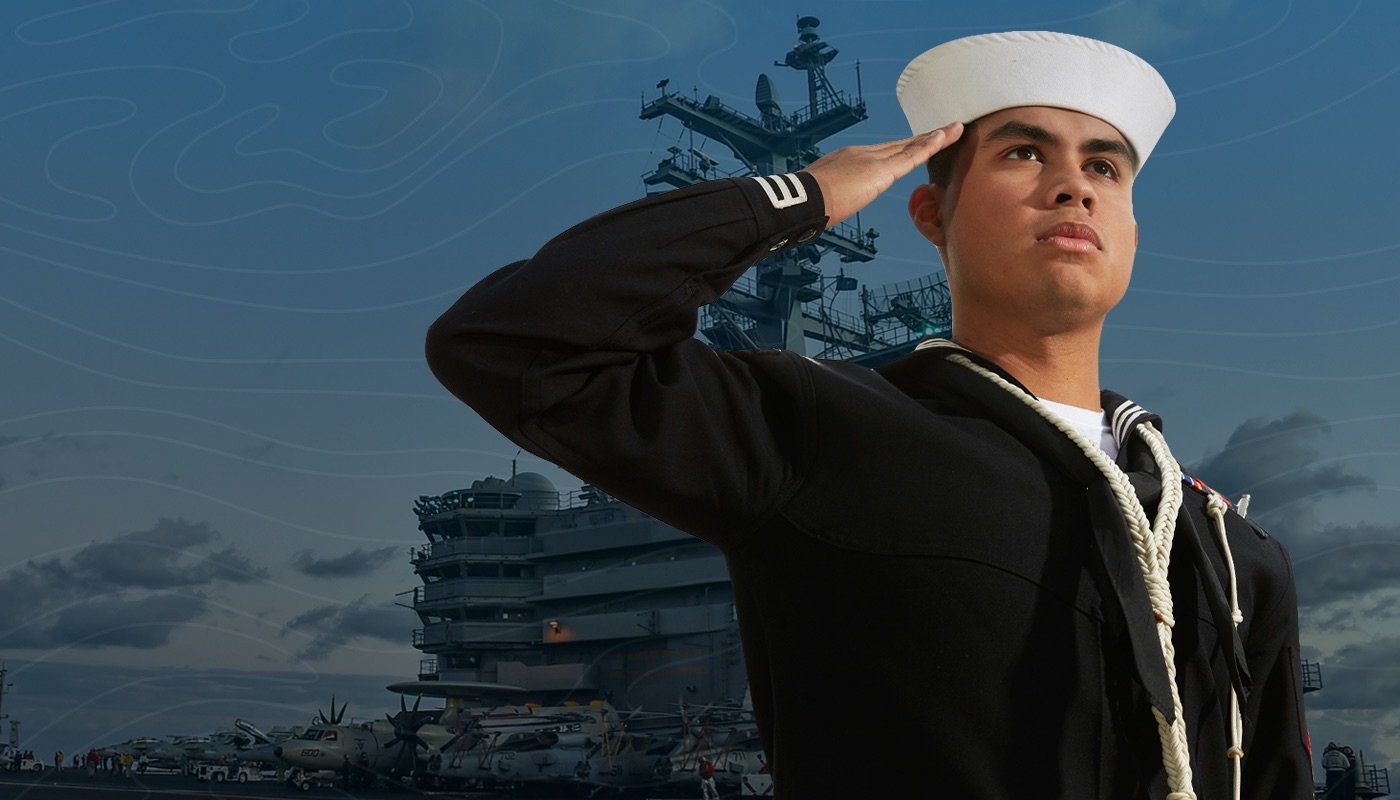 U.S. Navy Boatswain’s Mate salutes in his dress blue uniform while standing in front of a ship.