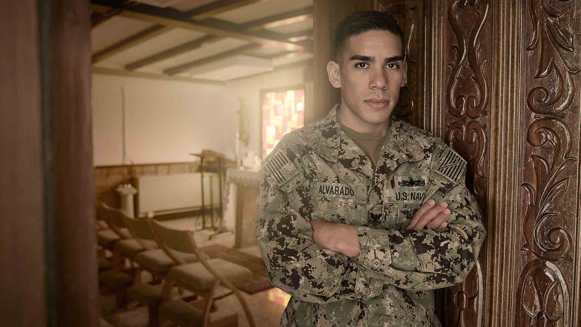 Navy Boatswain’s Mate Justin Alvarado poses for a photo in his family home wearing Navy fatigues